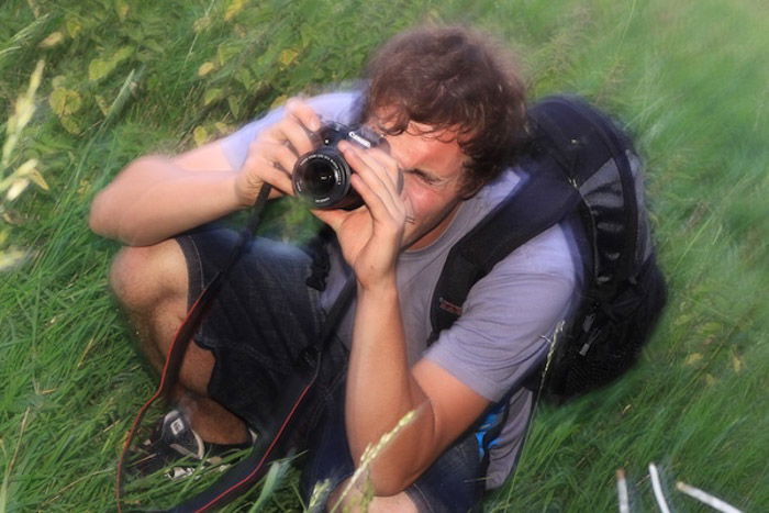 A blurry portrait of a photographer shooting with a DSLR outdoors