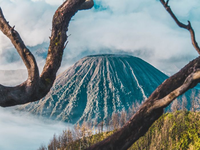 Foto de un volcán con ramas enmarcando el primer plano