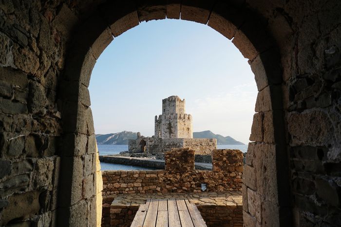 Un arco de piedra que enmarca un castillo y montañas al fondo