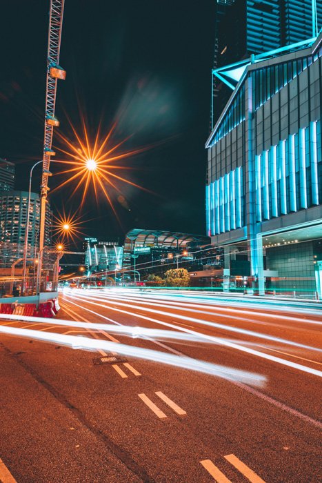 A cityscape with streaming light trails of cars whizzing by tall buildings