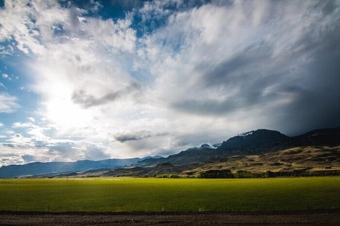 Photo of a green field with mountains in the back in sunny weather