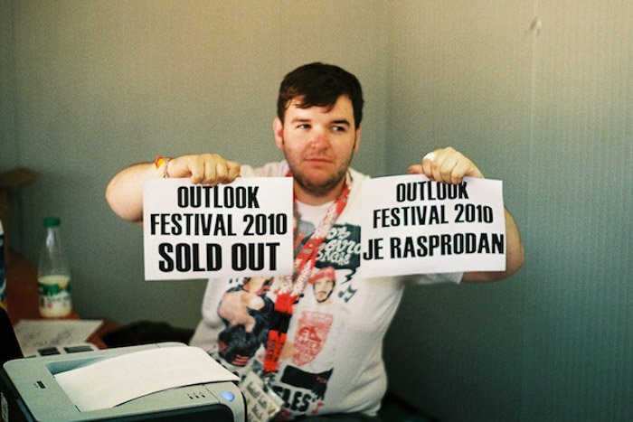 A man holding up two printed signs announcing a festival is sold out - photography balance 