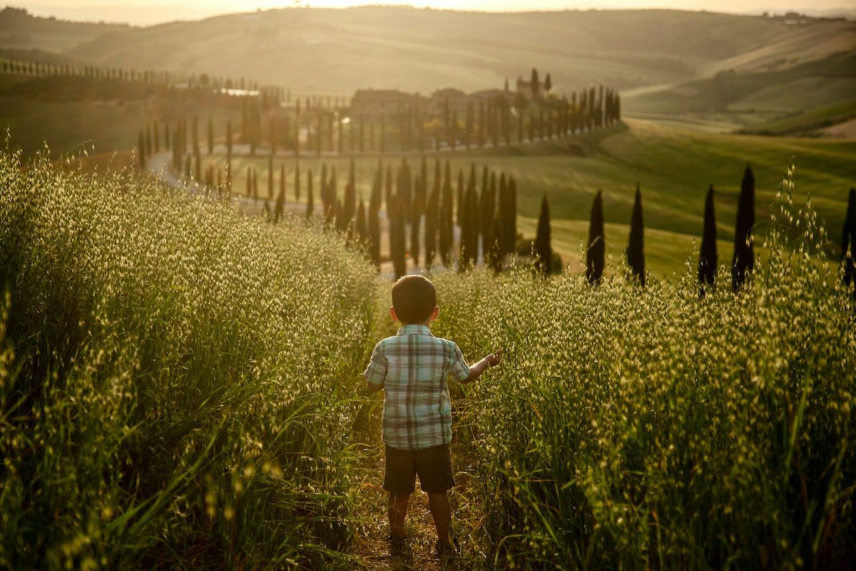 A boy walking down a path in the countryside surrounded by tall grass creating triangles in photography