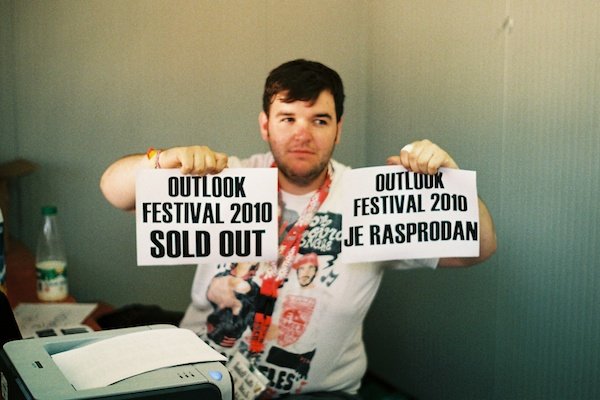 An overweight man holding up two pieces of paper saying: Outlook Festival 2010 sold out