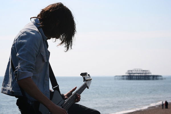 Foto de guitarrista masculino cantando en el escenario al aire libre con fondo oceánico