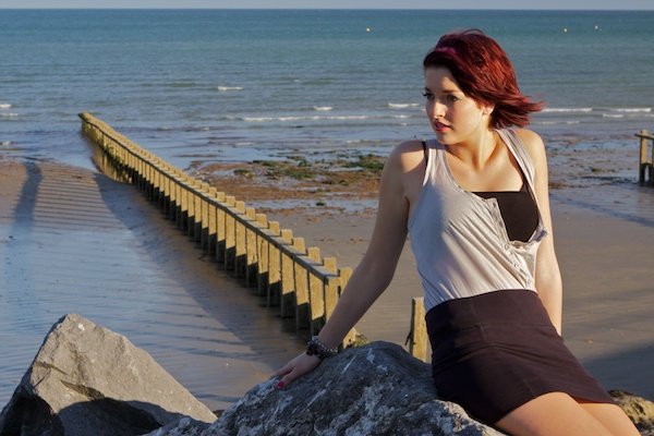 一名年轻女子坐在沙滩上的一块岩石上，看着镜头