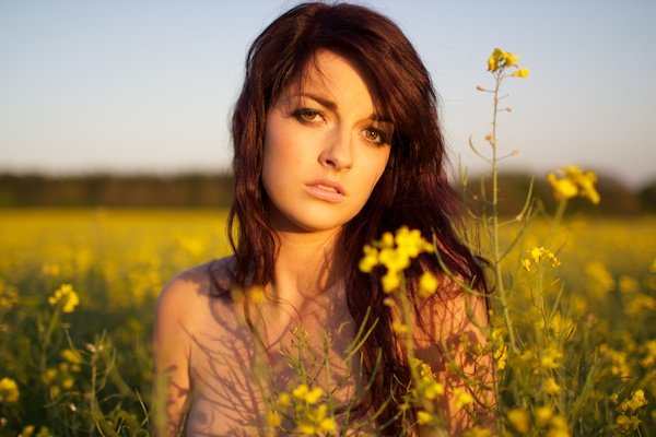 Photo of a young woman in the field of yellow flowers looking into the camera