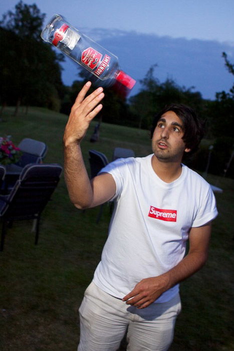 A man juggling a vodka bottle outdoors in low light - party photography