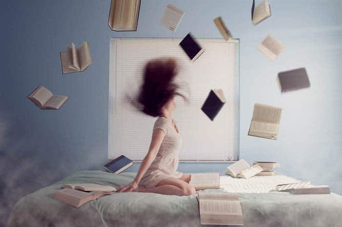 A conceptual portrait of a girl in her bedroom surrounded by flying books
