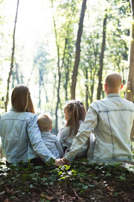 A bright and airy photo of a family sitting in the woods
