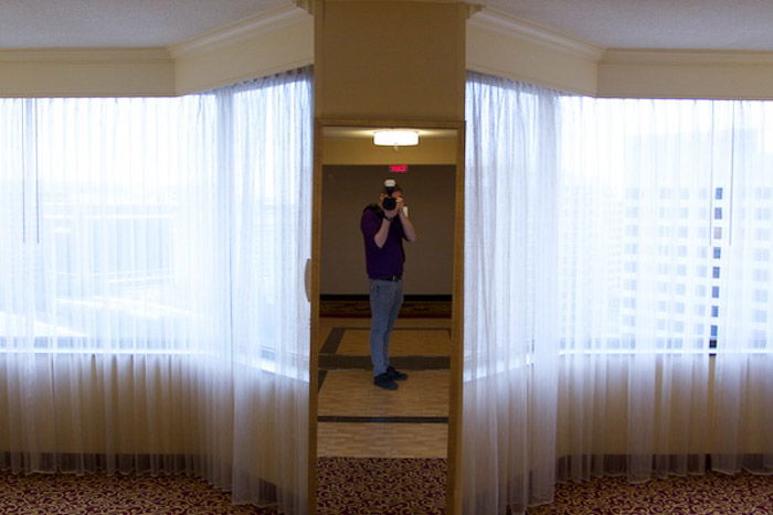 underexposed self-portrait in a mirror with bright curtains at each side to illustrate photography exposure tips