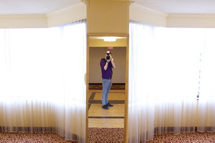 Overexposed self-portrait in a mirror with bright curtains at each side to illustrate photography exposure tips