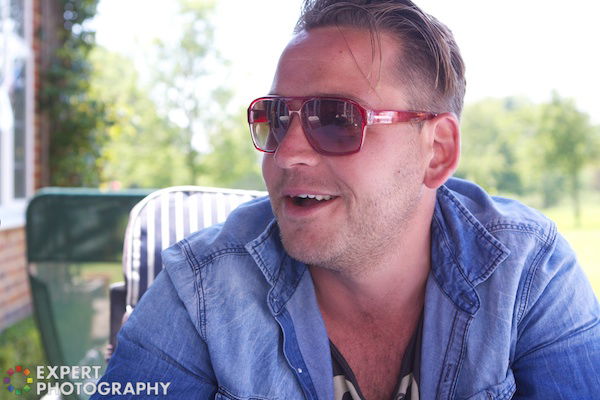 Man wearing a blue shirt and sunglasses looking to his right and smiling