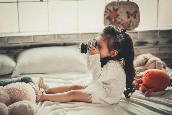 Cute little girl with a camera sitting on a bed