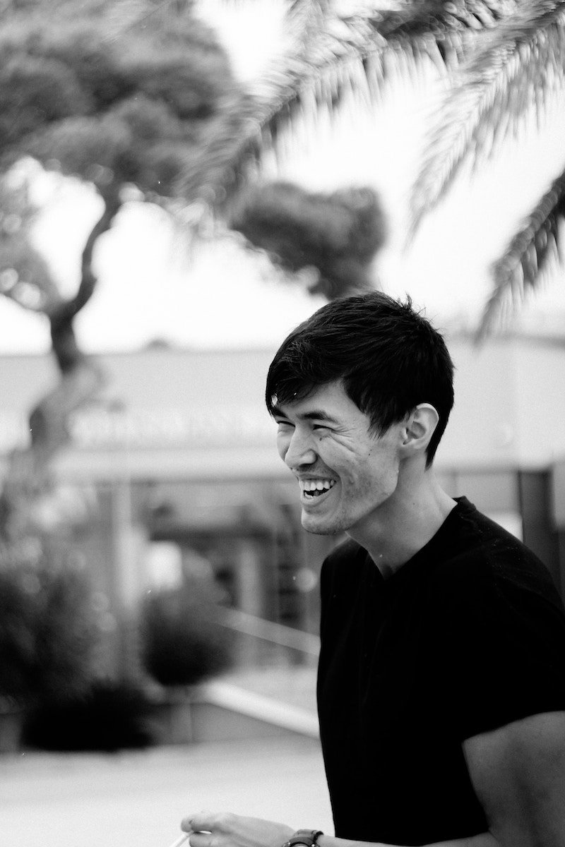 Black-and-white portrait of a man in a T-shirt outside laughing