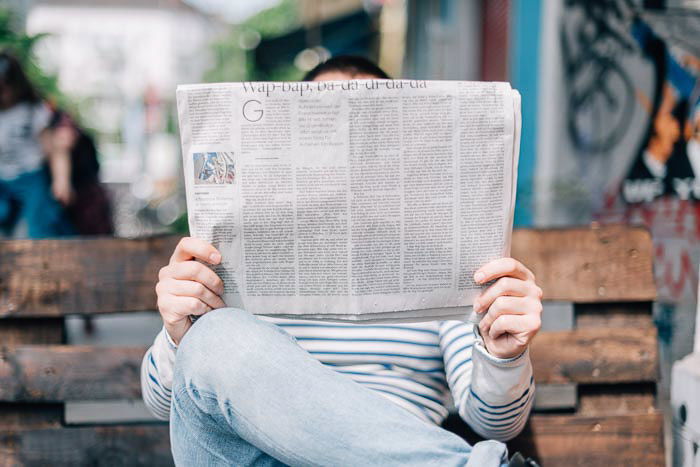 A straight on shot of a man sitting on a bench reading a newspaper