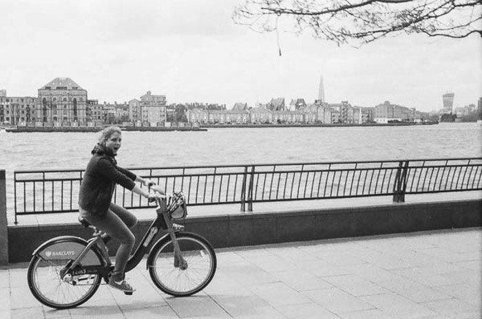Black and white shot of a girl cycling past a river, taken with the vintage camera Rollei B35