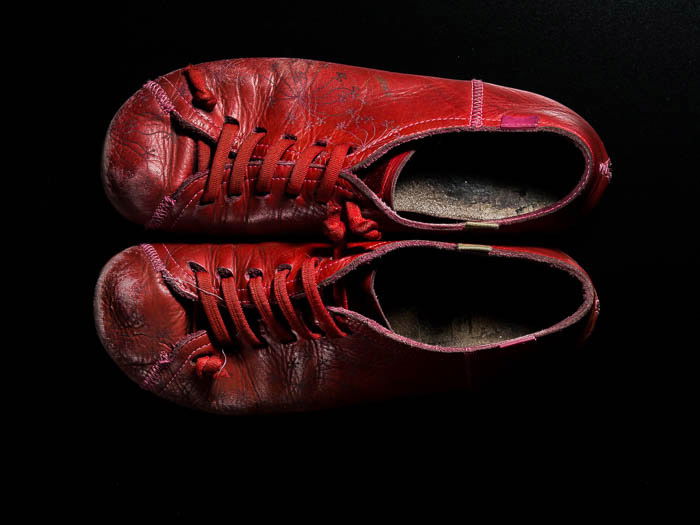 a pair of red camper shoes on black background