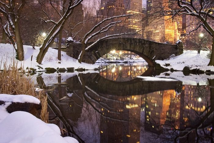A snow covered bridge over a river in the foreground of a cityscape as an example of creative landscape shots 