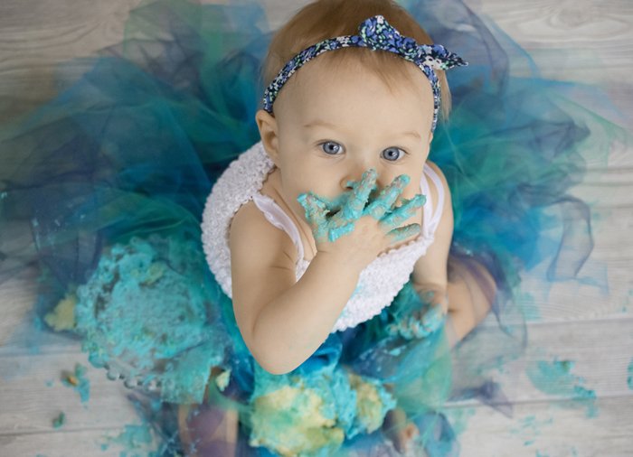 Cute portrait of a baby eating a green cake and looking up at the camera - DIY Cake Smash Photography