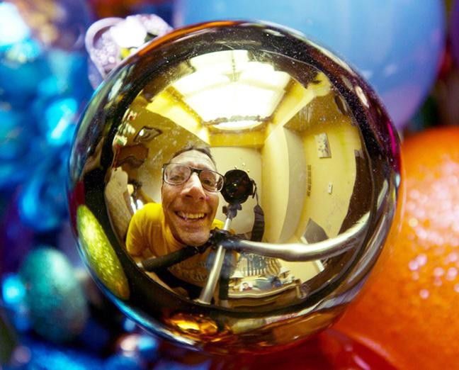 A photograph of a man seen in the reflection of a Christmas bauble - Photography Projects to Do with Children