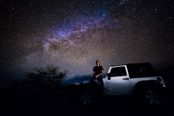 A Milky Way Photographer sitting on a car bonnet under a star filled sky