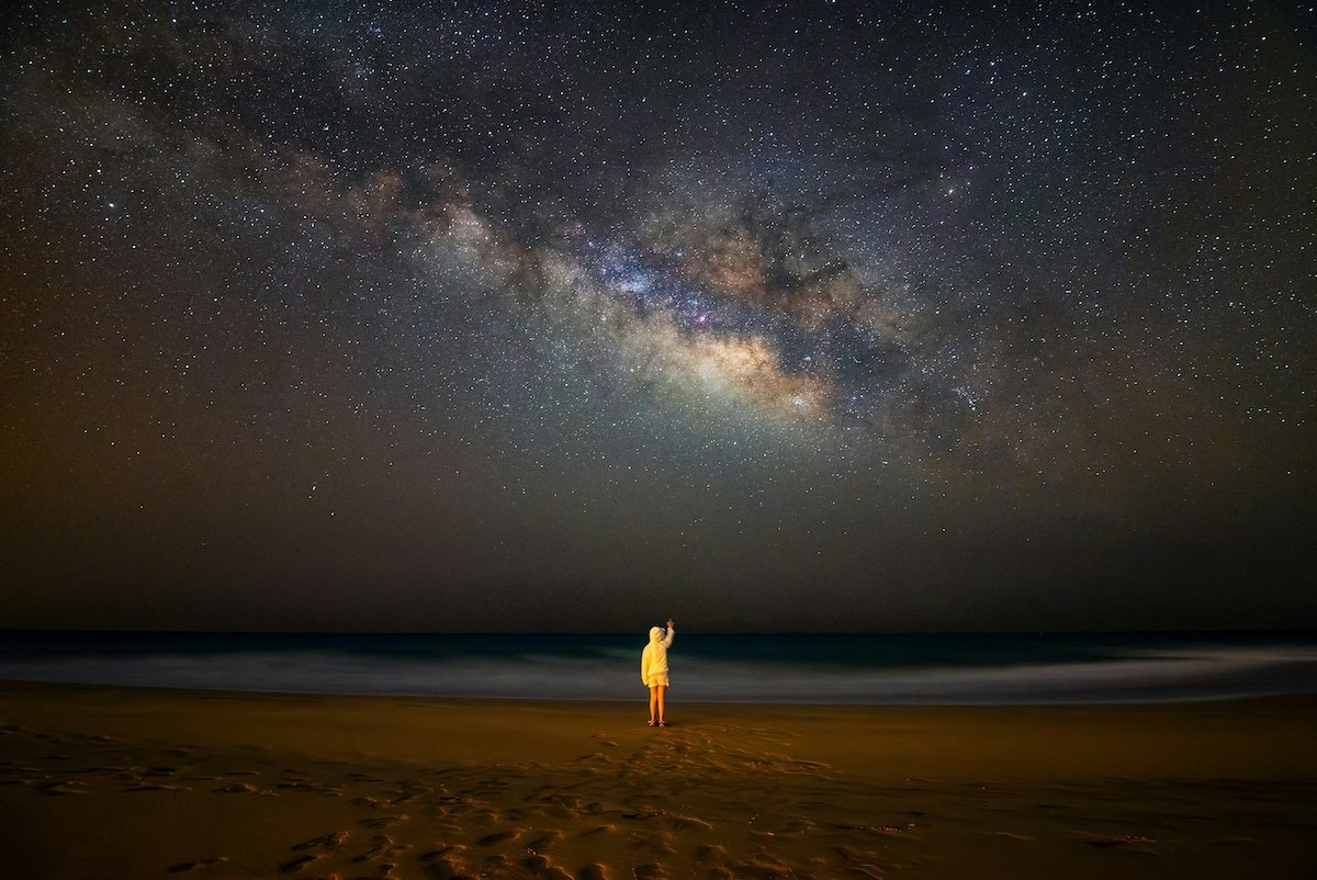 A child in a yellow coat standing under a beach under a starry sky taken with milky way photography gear