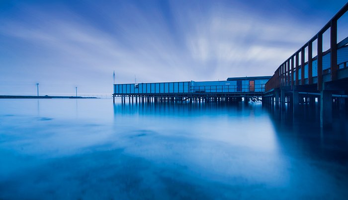 Natural blue monochrome long-exposure photo of boathouse on water