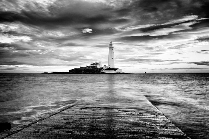 Black and white coastal view across the water looking towards a lighthouse, shot with a long exposure