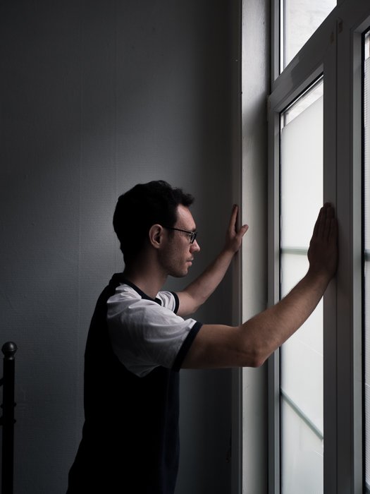 a portrait of a man gazing out a window, lit with subtle split lighting