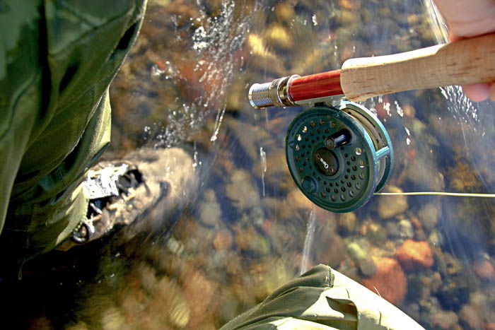 Artistic photo of a person fishing, showing the fishing rod and their boot