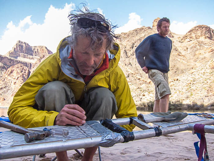 Adventure photography showing one man repairing a raft while another is standing in the background