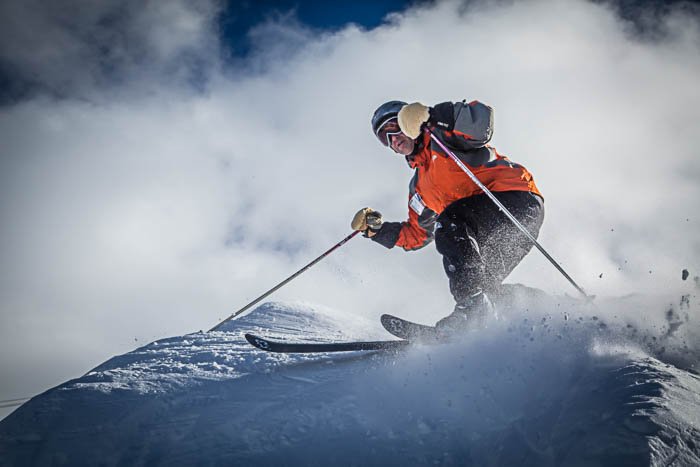 Picture of a skier turning, with powdered snow flying everywhere.