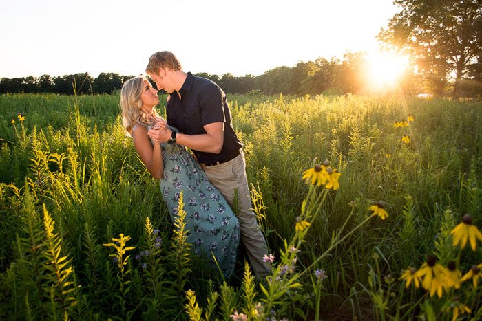 A man sweeps his girlfriend off her feet in a Golden Hour lit field in a calm countryside location