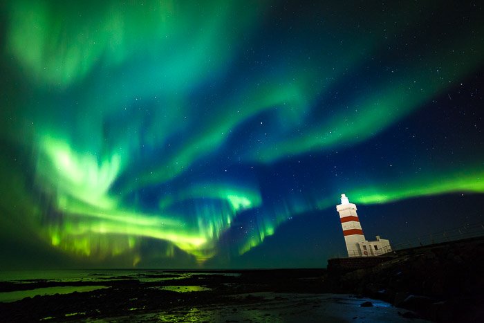 Northern lights picture with a lighthouse to the right, showing the Aurora Borealis colours