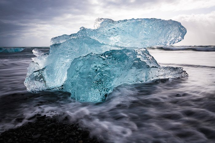 Escultura de hielo natural en forma de gran cristal azul, saliendo de las olas