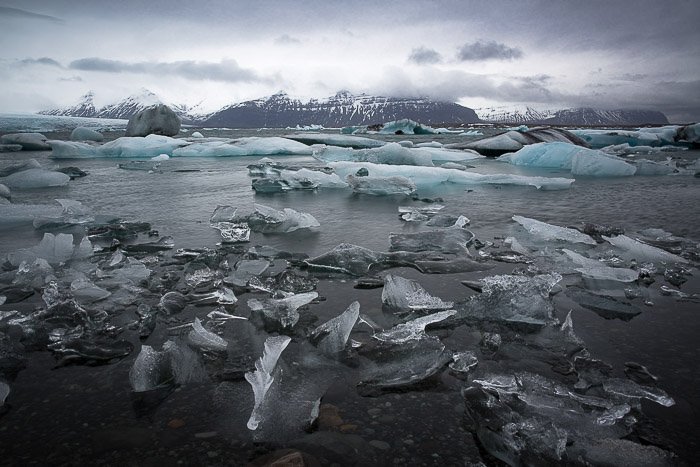 landscape picture of ice river with frozen pieces of ice floating in it and mountains in the distance, taken in Iceland