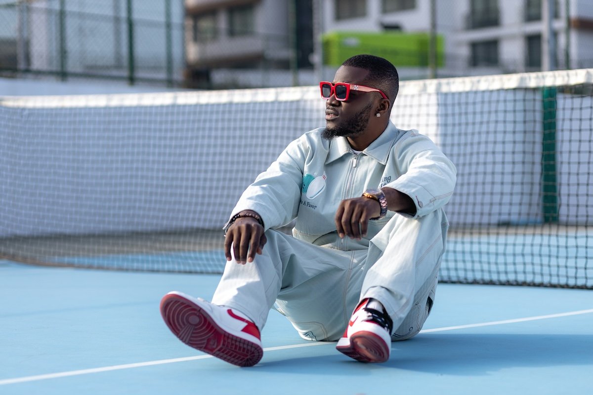 A man sitting on a tennis court with sunglasses on hiding eyeline in photography