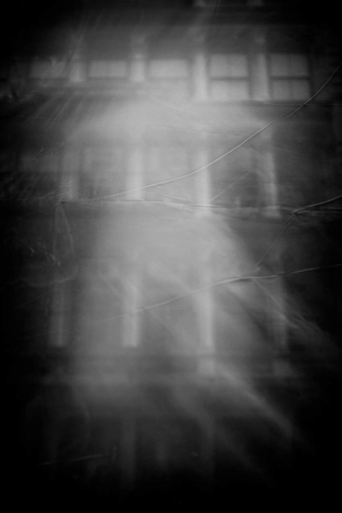 A ghostly haze is cast over the windows of a building in black and white street reflection photography.