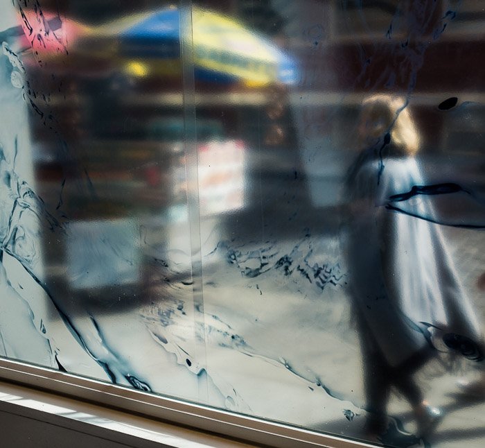 A passerby reflected in a street window. Color photography.