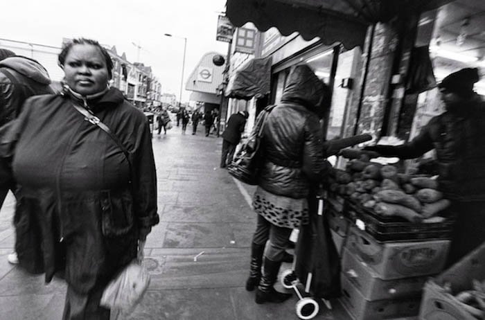 A street portrait of a woman walking down the street while others buy vegetables