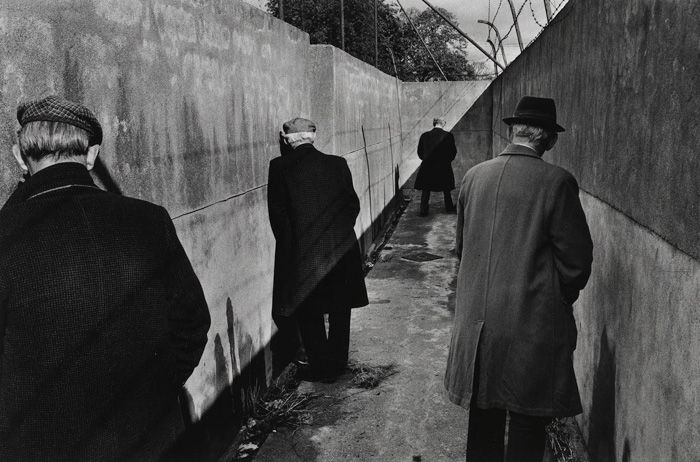 černobílá Pouliční fotografie čtyř mužů stojí v bezútěšné chodbě a močí 