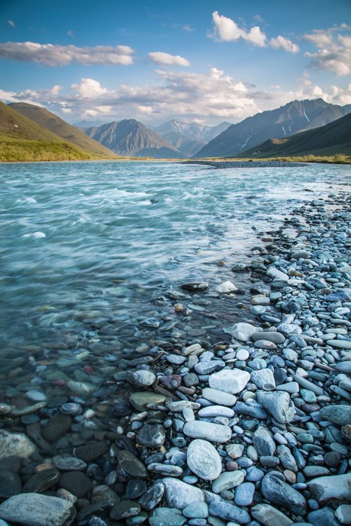 A river with rocks on its shore and mountains in the background