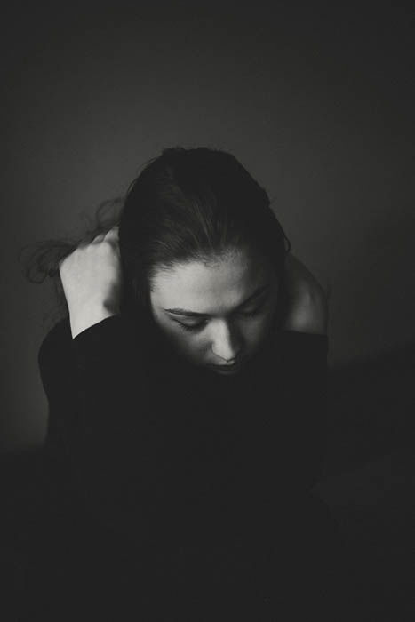 Atmospheric black and white portrait of a young woman hiding her head in her hands. Self portrait photography