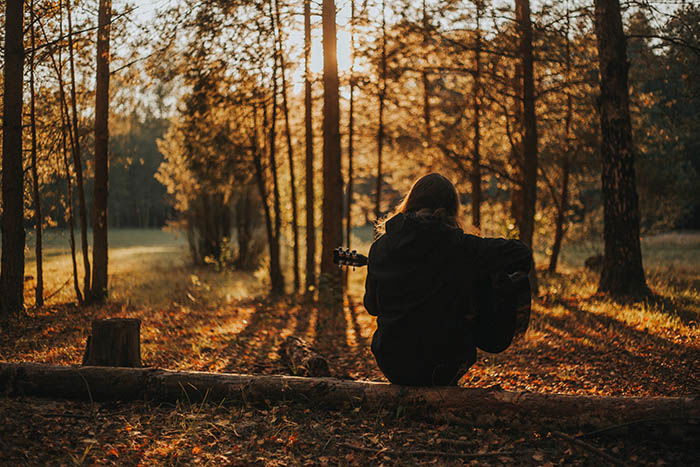 a girl playing guitar sitting on a log in a forest during fall, as a creative self-portrait photography idea