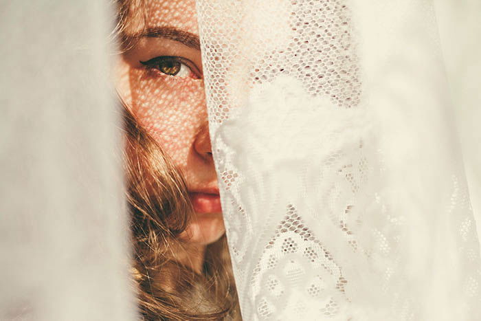 portrait of a girl hiding behind a white doily, only half of her face is visible