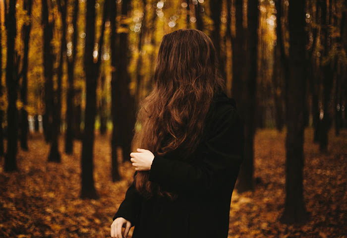 A woman dressed in black looking away from the photo, standing in a forest during autumn. Self portrait photography