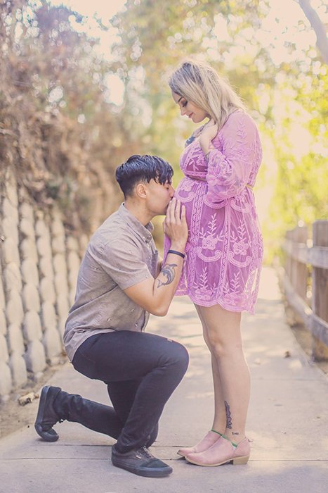 photo of a pregnant couple with the man kneeling in front of the woman, kissing her belly