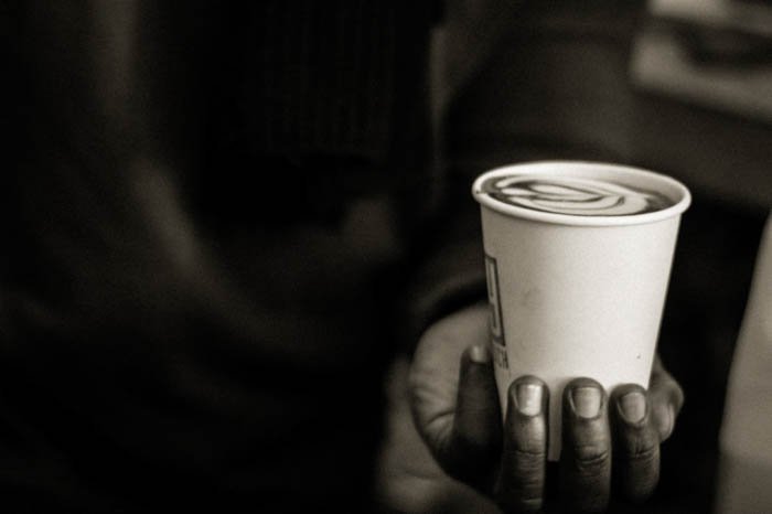 一个人的手拿着一个白色塑料咖啡杯的近距离照片。创意拿铁咖啡的设计是可见的。