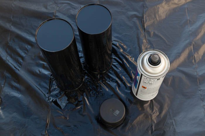 Two Pringles chips cans painted black and a black spray paint can to make a DIY speedlite modifier